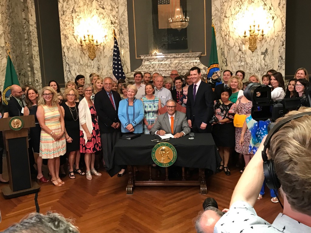 Washington Governor Jay Inslee signs paid family and medical leave into law surrounded by legislators, advocates, and business owners, July 5, 2017.